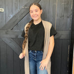 black shirt, beige cardigan, and blue jeans standing in front of a dark wooden door.