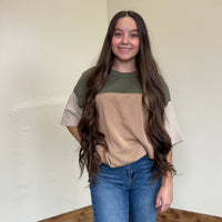 Woman wearing a two-tone shirt and jeans standing in a room with a neutral wall.