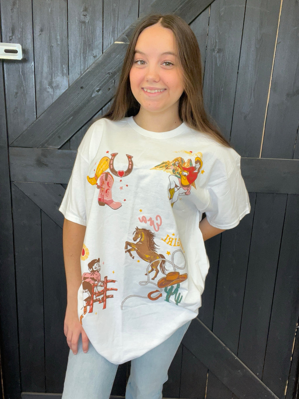 Person wearing a white t-shirt with colorful graphics in front of a wooden door.