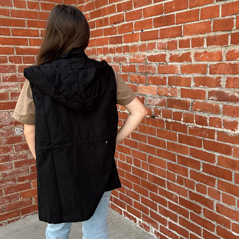 Person wearing a black vest against a red brick wall