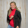 Woman wearing a red turtleneck and black cardigan in front of a store with clothing racks.