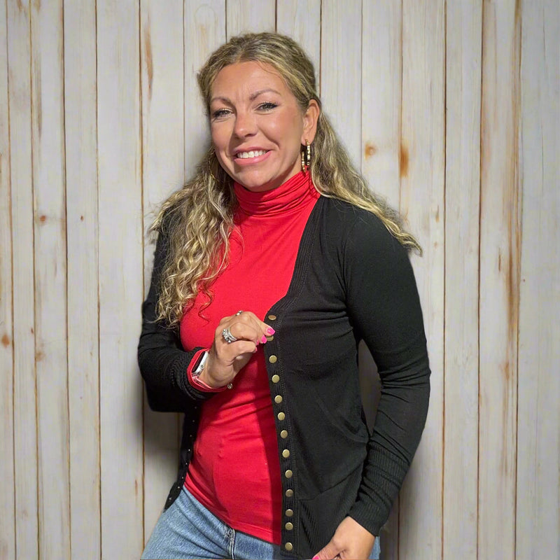Woman wearing a red turtleneck and black cardigan in front of a store with clothing racks.