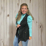 Woman posing in a clothing store with a rack of clothes and a yellow chair in the background.