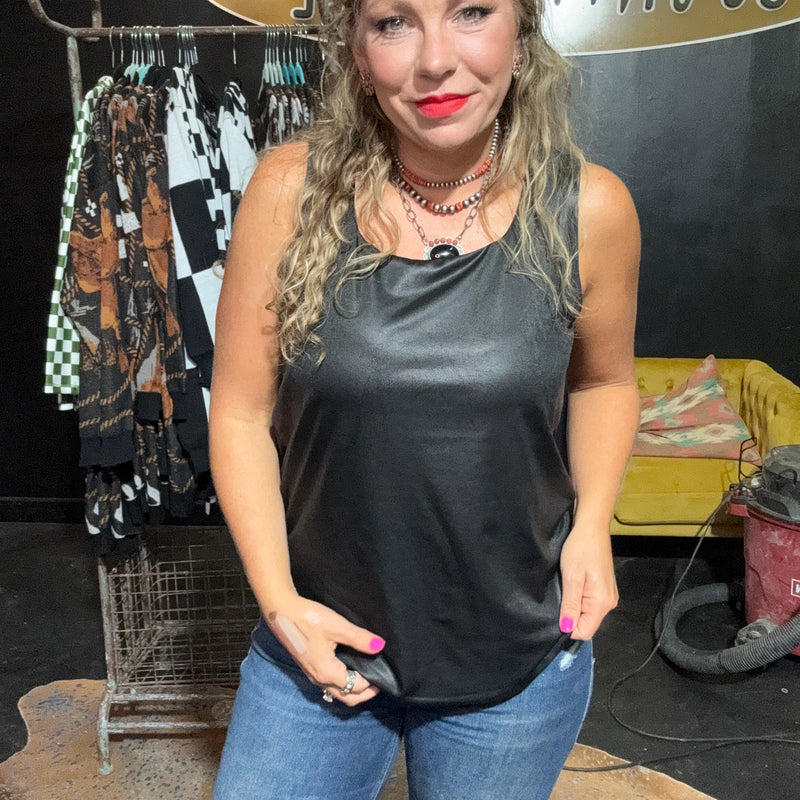 Woman wearing a black sleeveless top and blue jeans standing in a room with clothing racks and a vacuum cleaner.