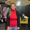 Woman wearing a red shirt and black cardigan in front of a store with clothing racks and a yellow chair.