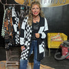 Woman wearing a black and white checkered cardigan in a room with clothing racks and a yellow chair.