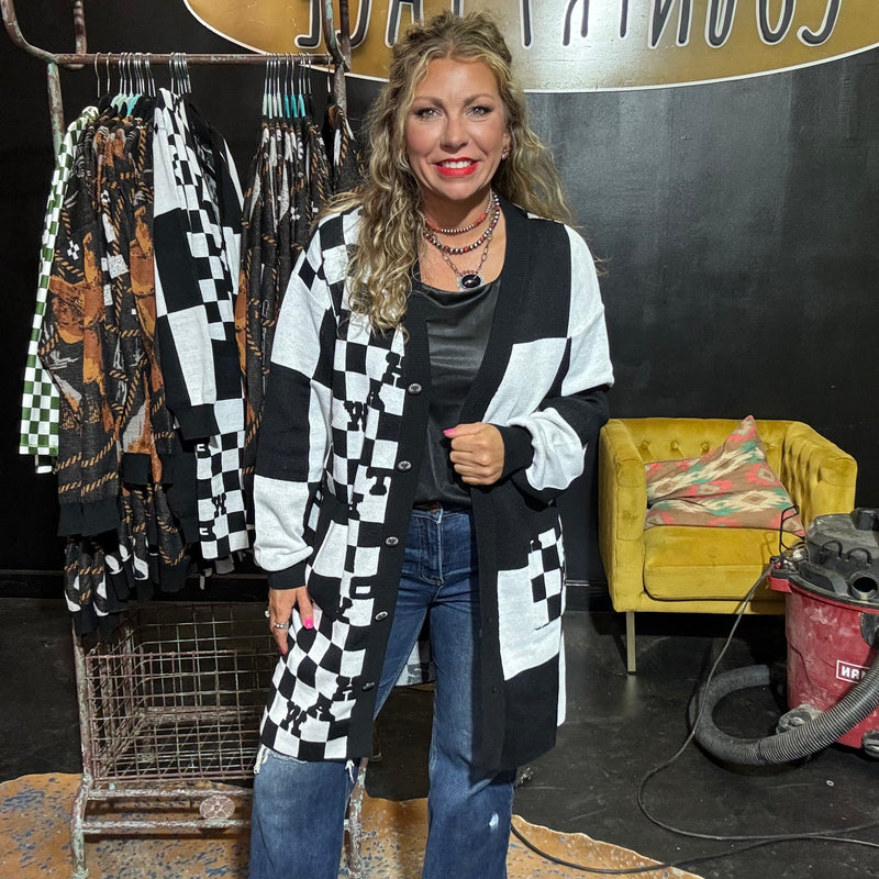 Woman wearing a black and white checkered cardigan in a room with clothing racks and a yellow chair.