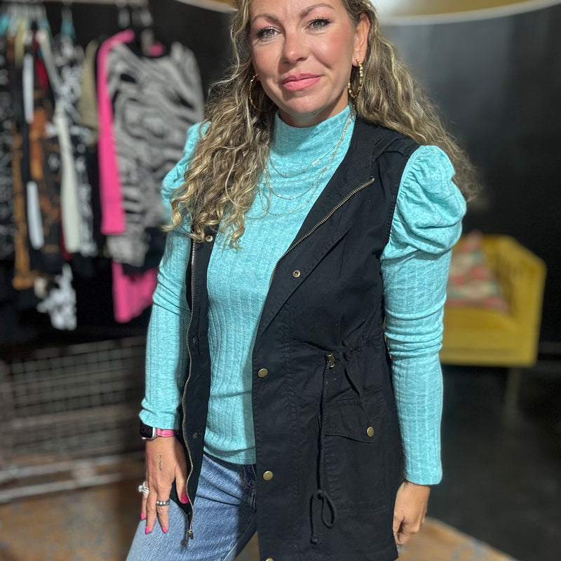 Woman wearing a black vest over a light blue sweater with a blurred background