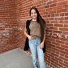 Woman standing against a brick wall wearing a brown top and light blue jeans.