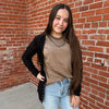 Person standing against a brick wall wearing a beige top and light blue jeans.