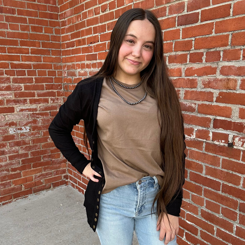 Person standing against a brick wall wearing a beige top and light blue jeans.