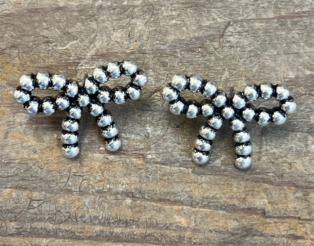 Pair of silver bow-shaped earrings on a wooden surface