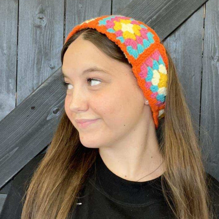 Person wearing a colorful crocheted headband against a wooden background