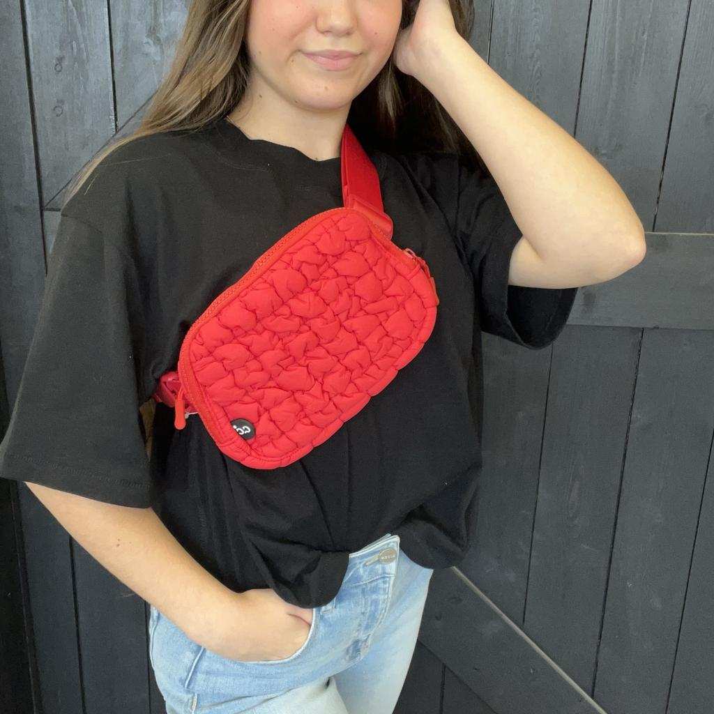 Person wearing a black shirt with a red quilted bag over one shoulder against a wooden background