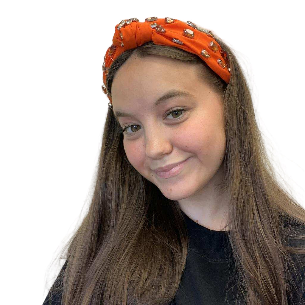 Person wearing an orange headband with decorative elements on a plain background