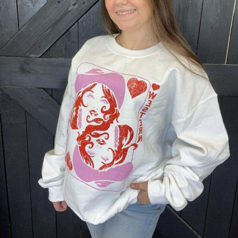 Person wearing a white sweatshirt with a graphic design in front of a wooden door.