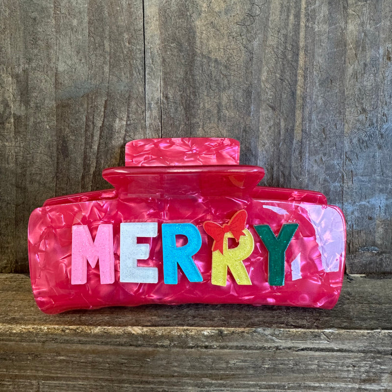 Pink clutch with colorful letters spelling 'MERRY' on a wooden surface