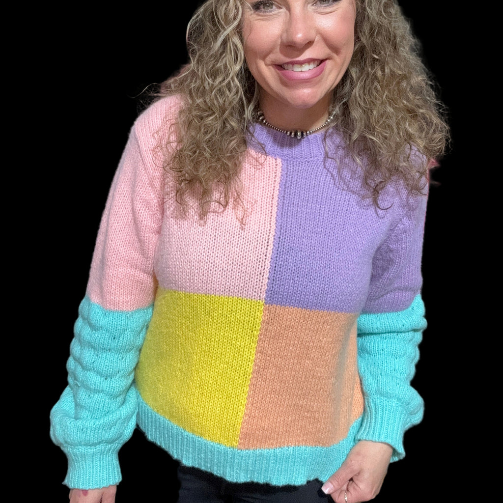 A woman wearing a long sleeve sweater with pastel color blocks, including pink, purple, yellow, and blue.