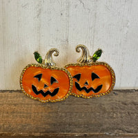 Pair of jack-o'-lantern earrings on a wooden surface with a neutral background