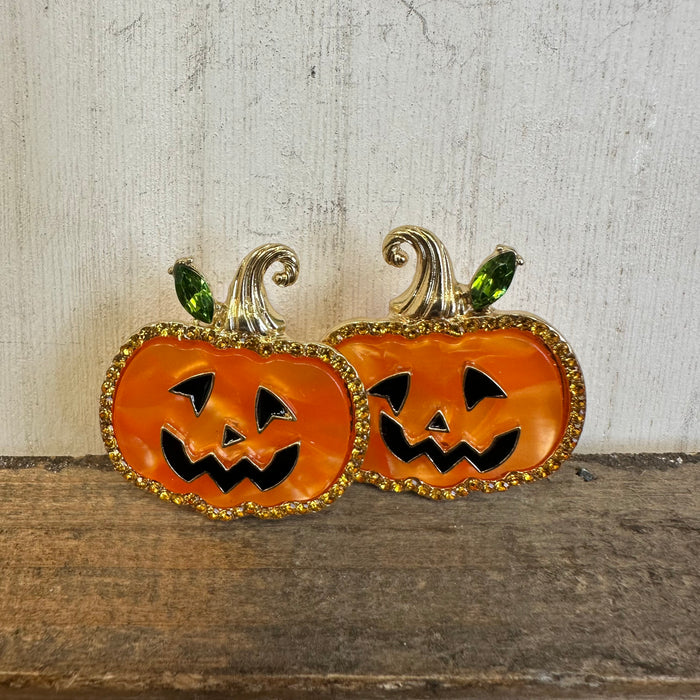 Pair of jack-o'-lantern earrings on a wooden surface with a neutral background