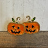 Pair of jack-o'-lantern earrings on a wooden surface with a neutral background