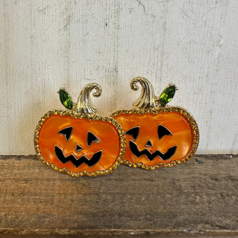 Pair of jack-o'-lantern earrings on a wooden surface with a neutral background