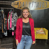 Woman standing in a store with clothing racks and a yellow couch in the background.