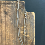 Silver chain necklace on a wooden block with a dark background