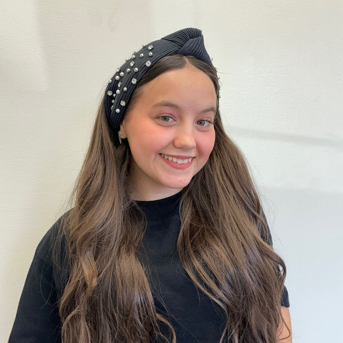 Young girl wearing a black headband with pearls against a white background