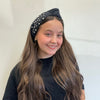 Young girl wearing a black headband with pearls against a white background