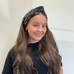 Young girl wearing a black headband with pearls against a white background