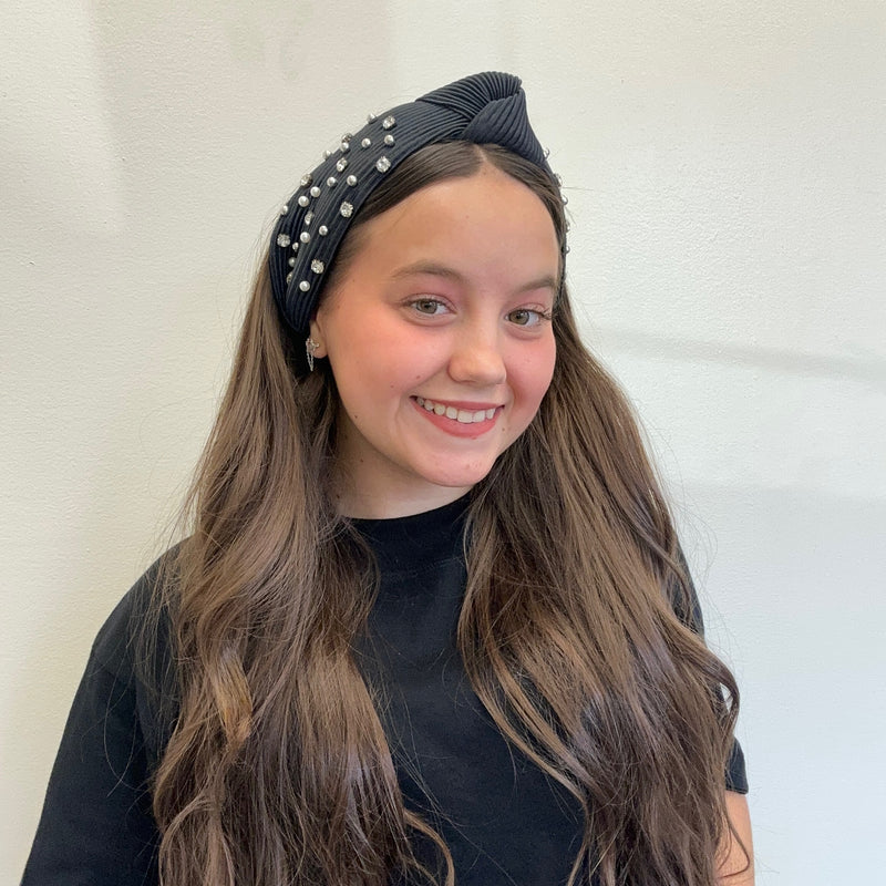 Young girl wearing a black headband with pearls against a white background