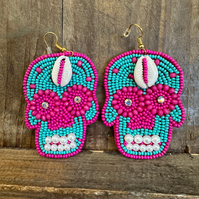 Pair of beaded skull earrings with turquoise and pink colors on a wooden background